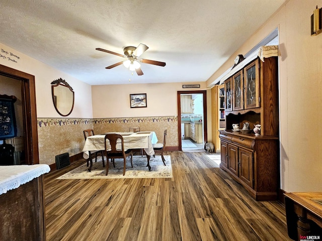 dining space featuring dark wood-style flooring, visible vents, a ceiling fan, wainscoting, and a textured ceiling