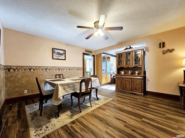 dining space featuring a wainscoted wall, ceiling fan, a textured ceiling, and dark wood-type flooring