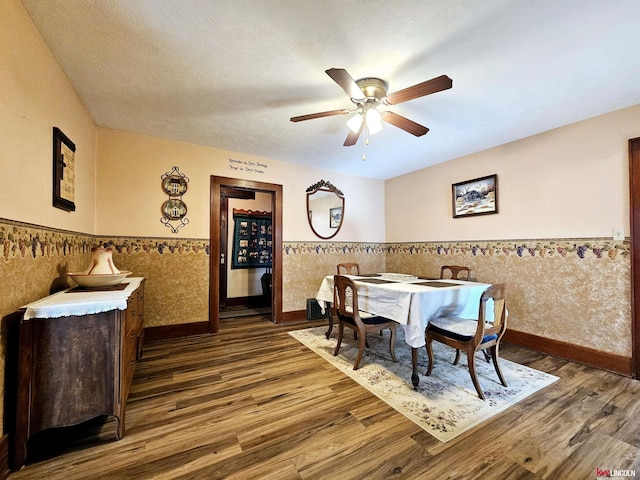 dining area featuring dark wood-style floors, wainscoting, ceiling fan, and a textured ceiling