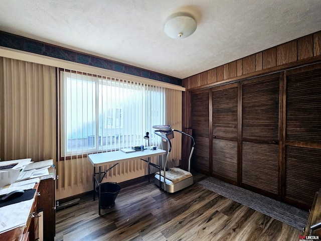 home office featuring wooden walls, a textured ceiling, and dark wood-style flooring