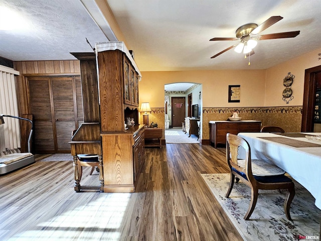 bedroom with arched walkways, dark wood finished floors, a ceiling fan, wainscoting, and a textured ceiling