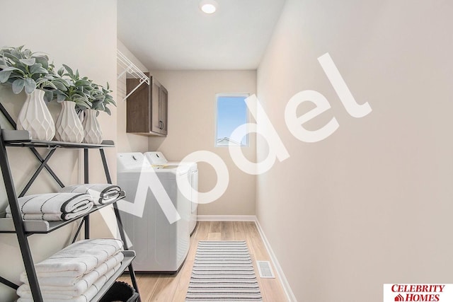 laundry area featuring cabinets, washing machine and clothes dryer, and light hardwood / wood-style flooring