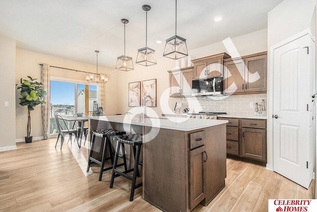 kitchen with decorative light fixtures, light hardwood / wood-style flooring, a center island with sink, a kitchen breakfast bar, and backsplash