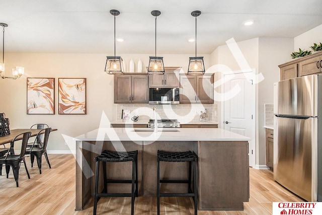 kitchen featuring appliances with stainless steel finishes, decorative backsplash, hanging light fixtures, a kitchen island with sink, and light hardwood / wood-style floors