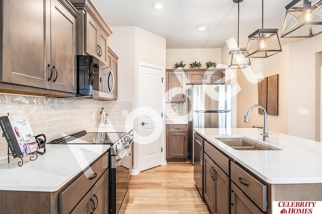 kitchen with sink, light hardwood / wood-style flooring, appliances with stainless steel finishes, light stone counters, and decorative light fixtures