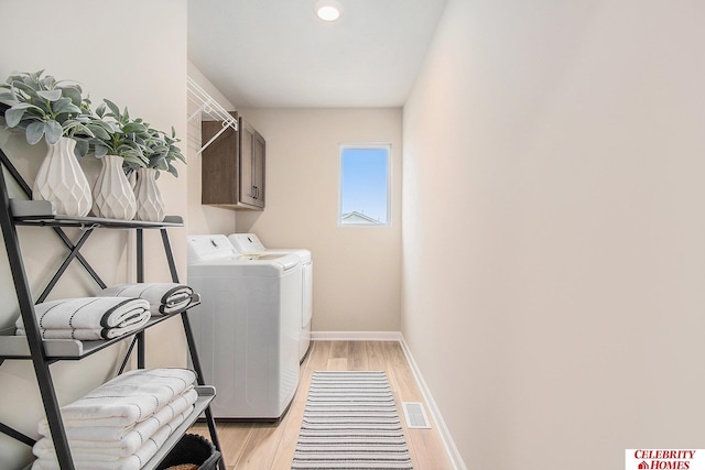 clothes washing area with washer and dryer, cabinets, and light wood-type flooring