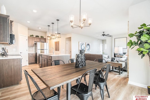 dining room featuring ceiling fan with notable chandelier, sink, and light wood-type flooring