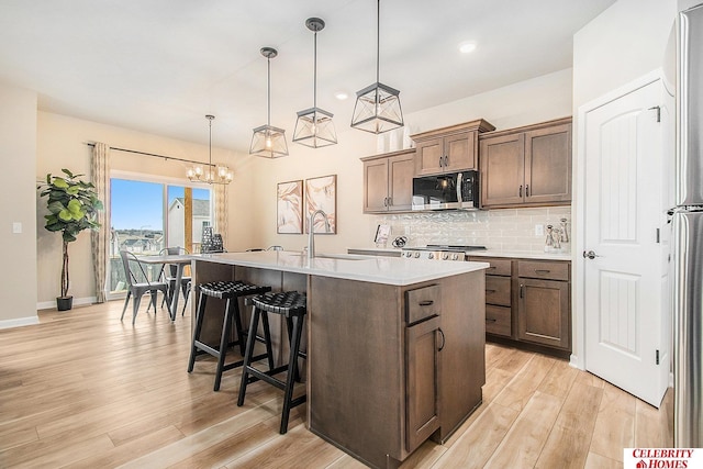 kitchen featuring stainless steel appliances, an island with sink, pendant lighting, and light hardwood / wood-style flooring