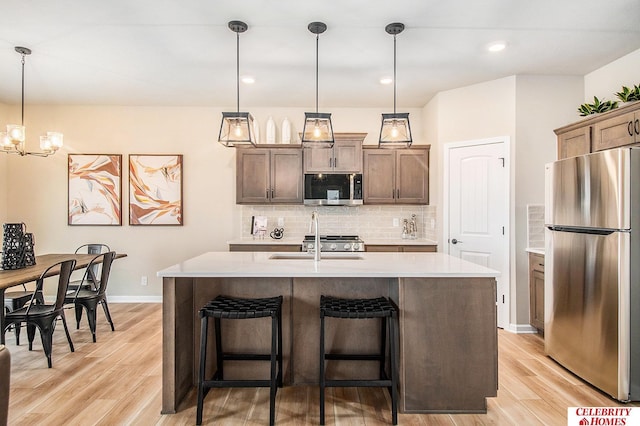 kitchen with pendant lighting, sink, light hardwood / wood-style flooring, appliances with stainless steel finishes, and a center island with sink