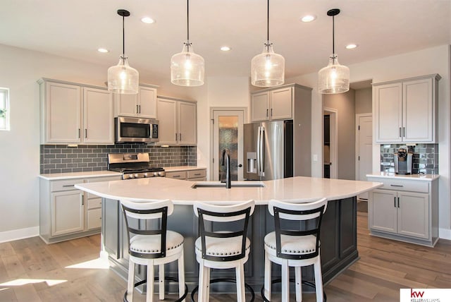 kitchen with appliances with stainless steel finishes, decorative light fixtures, tasteful backsplash, an island with sink, and sink