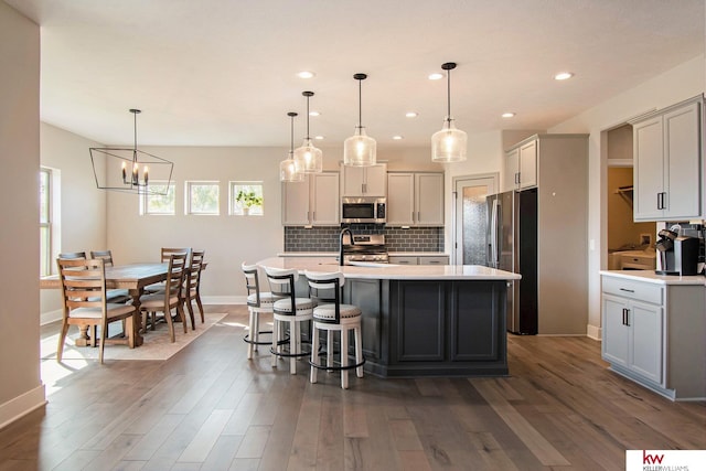 kitchen featuring appliances with stainless steel finishes, dark hardwood / wood-style floors, pendant lighting, a kitchen breakfast bar, and a center island with sink