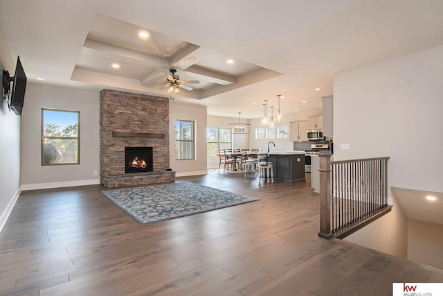 living room with ceiling fan with notable chandelier, a fireplace, beamed ceiling, coffered ceiling, and dark wood-type flooring