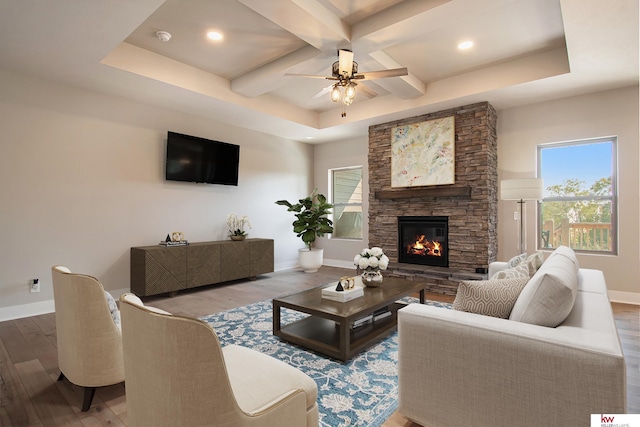 living room with coffered ceiling, ceiling fan, a stone fireplace, and hardwood / wood-style floors