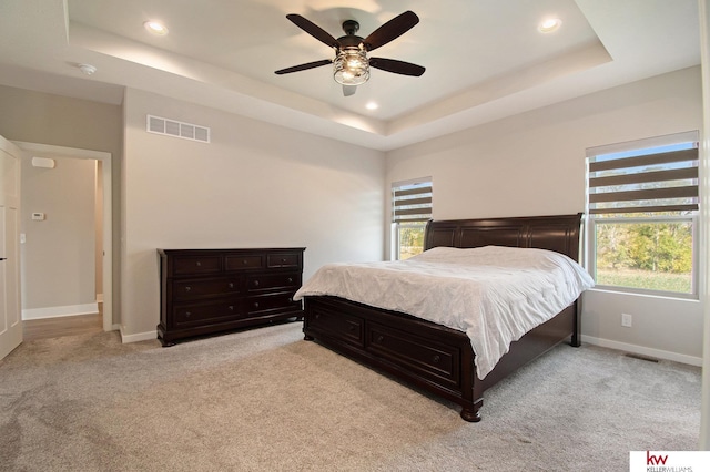 bedroom with multiple windows, ceiling fan, and a tray ceiling