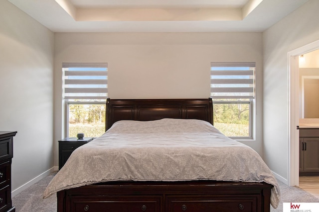 bedroom featuring ensuite bath, a raised ceiling, and light colored carpet