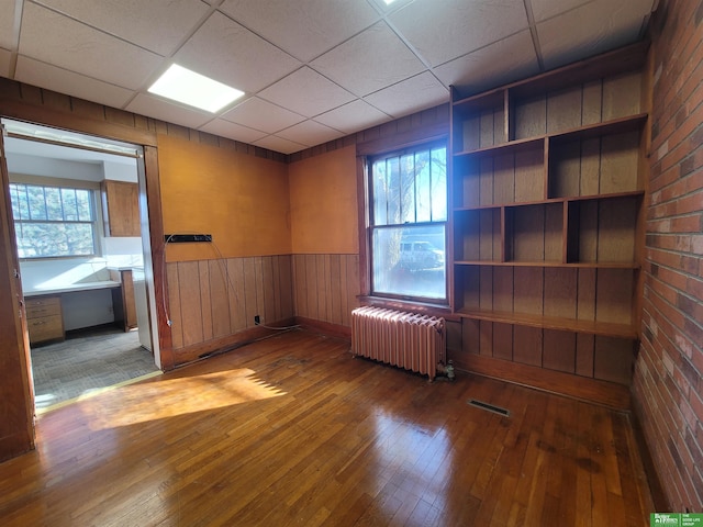 empty room with a paneled ceiling, radiator heating unit, and wood-type flooring