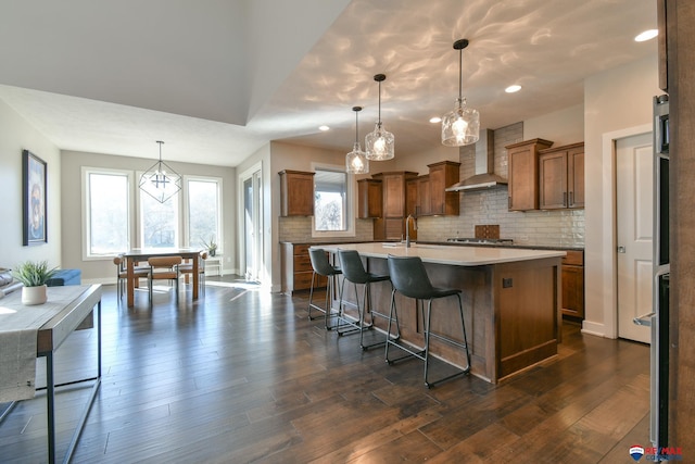 kitchen with wall chimney exhaust hood, decorative light fixtures, a breakfast bar, and a center island with sink