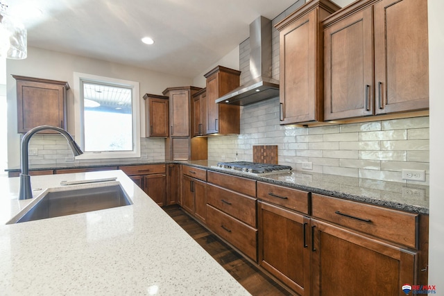 kitchen featuring dark wood-type flooring, stainless steel gas cooktop, sink, light stone countertops, and wall chimney range hood