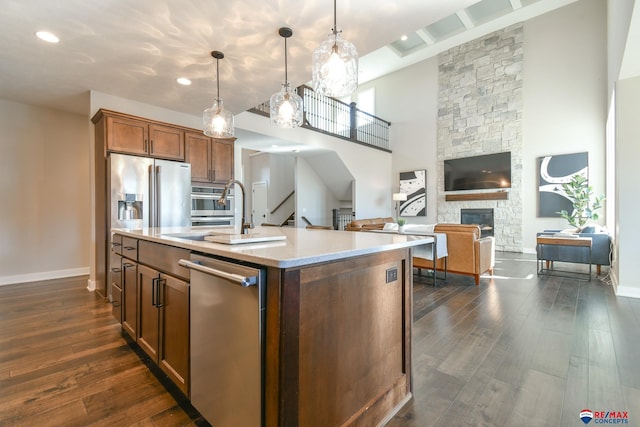 kitchen with sink, dark wood-type flooring, a kitchen island with sink, stainless steel appliances, and decorative light fixtures