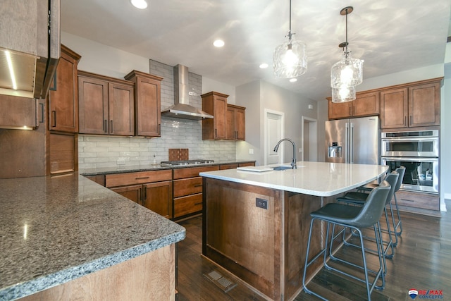 kitchen with wall chimney range hood, sink, a breakfast bar area, appliances with stainless steel finishes, and hanging light fixtures