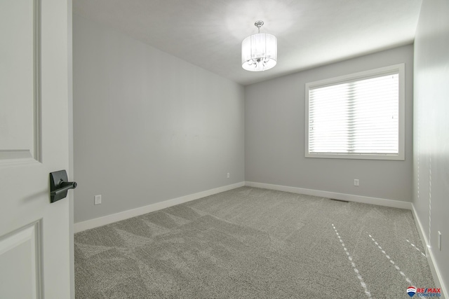 carpeted spare room featuring a notable chandelier