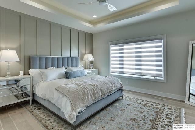 bedroom featuring ceiling fan, light wood-type flooring, and a tray ceiling