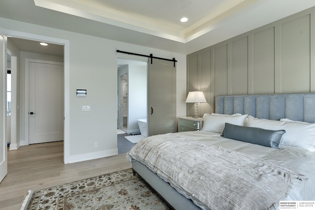 bedroom with a raised ceiling, a barn door, and light hardwood / wood-style floors