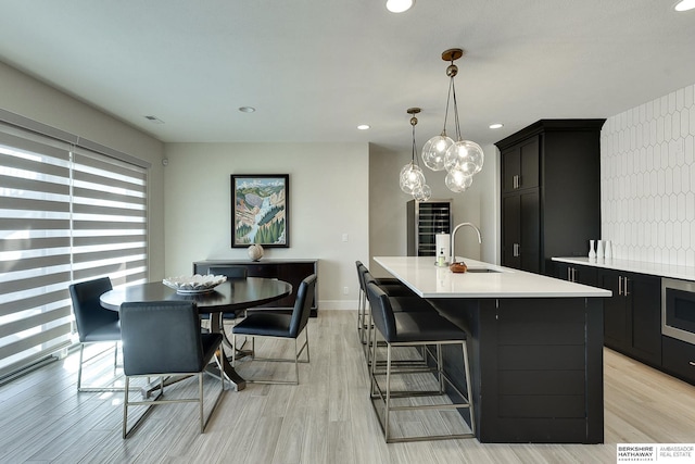 kitchen featuring pendant lighting, a breakfast bar area, light hardwood / wood-style floors, and a center island with sink