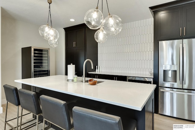 kitchen featuring a breakfast bar area, a kitchen island with sink, sink, and stainless steel fridge with ice dispenser