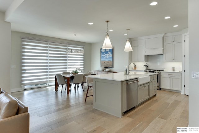 kitchen featuring pendant lighting, sink, light hardwood / wood-style flooring, appliances with stainless steel finishes, and a center island with sink