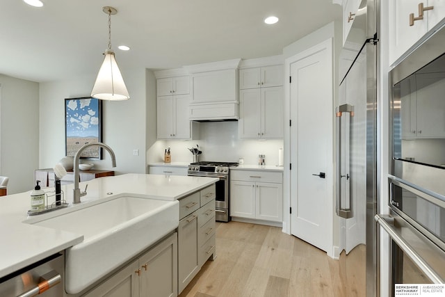 kitchen with sink, light hardwood / wood-style flooring, hanging light fixtures, stainless steel appliances, and white cabinets