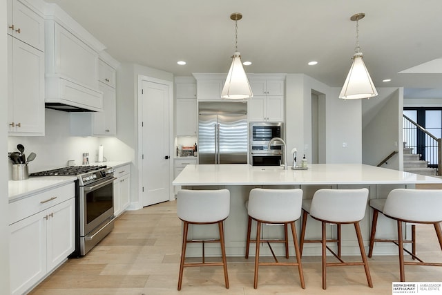 kitchen featuring white cabinetry, a kitchen island with sink, built in appliances, and decorative light fixtures