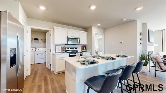 kitchen featuring a breakfast bar area, white cabinets, washing machine and clothes dryer, stainless steel appliances, and a center island with sink