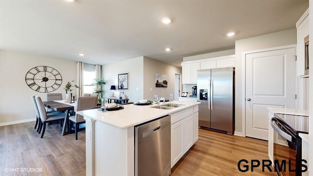 kitchen with appliances with stainless steel finishes, an island with sink, sink, white cabinets, and light hardwood / wood-style flooring