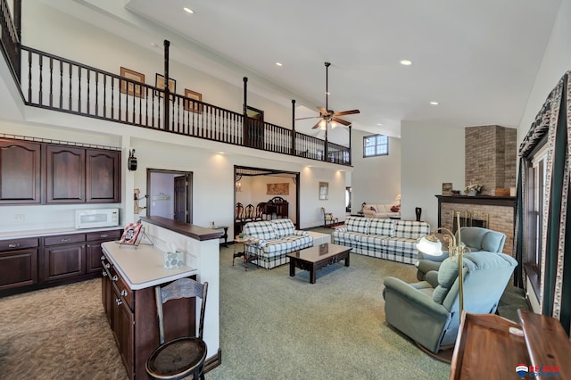 living area featuring a high ceiling, a fireplace, a ceiling fan, and light colored carpet