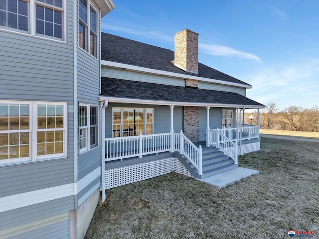 exterior space with covered porch, a shingled roof, a chimney, and a lawn