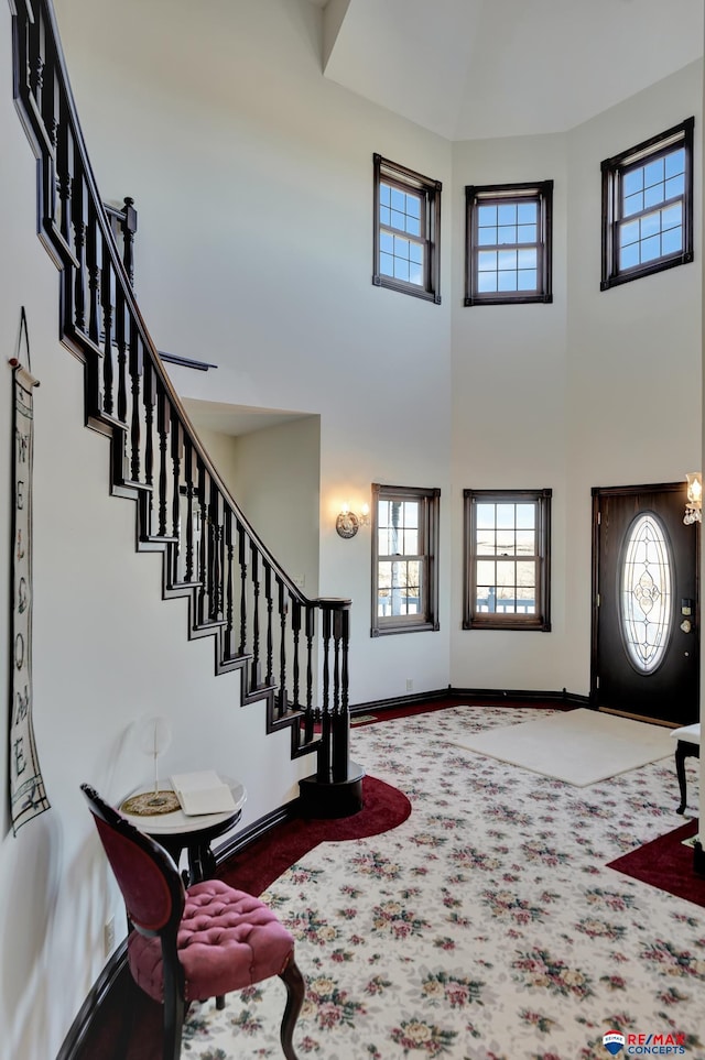 foyer featuring a towering ceiling, baseboards, stairway, and carpet flooring