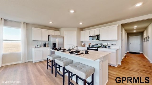 kitchen with stainless steel appliances, white cabinets, and a center island with sink