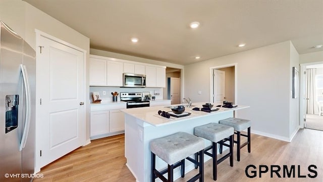 kitchen with a kitchen island with sink, white cabinetry, stainless steel appliances, a kitchen bar, and light wood-type flooring