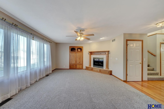 unfurnished living room with hardwood / wood-style floors, a tile fireplace, and ceiling fan