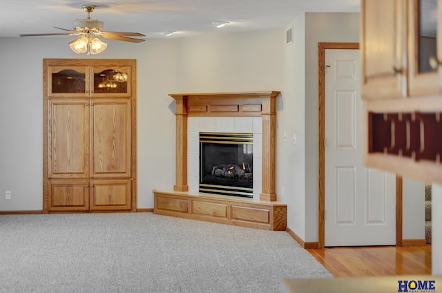 unfurnished living room with a tiled fireplace, light carpet, and ceiling fan