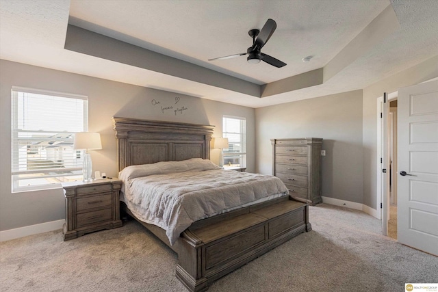 bedroom with a raised ceiling, ceiling fan, light colored carpet, and a textured ceiling