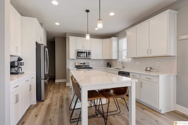 kitchen featuring sink, white cabinetry, stainless steel appliances, light stone counters, and decorative light fixtures