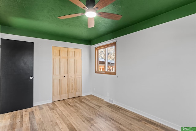 unfurnished bedroom featuring a textured ceiling, light hardwood / wood-style flooring, a closet, and ceiling fan