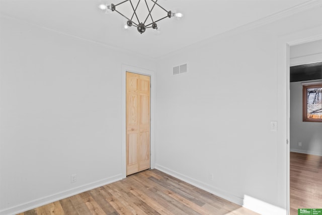 empty room with crown molding, a chandelier, and light wood-type flooring