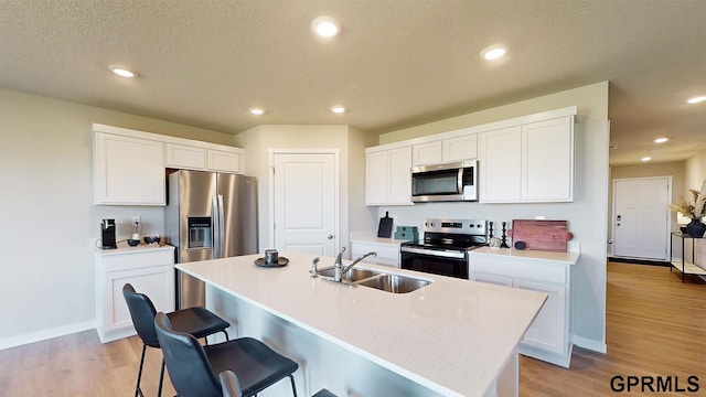 kitchen featuring sink, white cabinetry, stainless steel appliances, light hardwood / wood-style floors, and a center island with sink