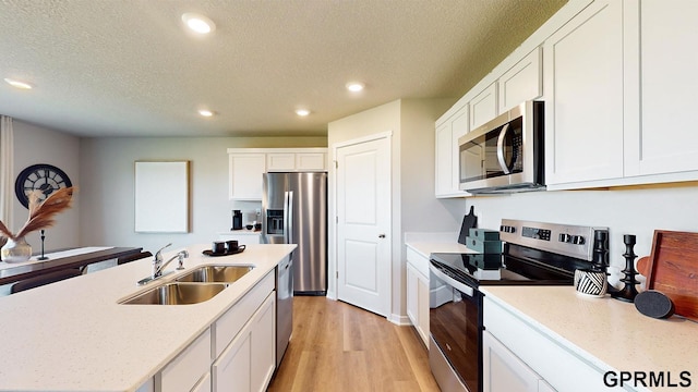 kitchen featuring sink, white cabinetry, a textured ceiling, appliances with stainless steel finishes, and light hardwood / wood-style floors