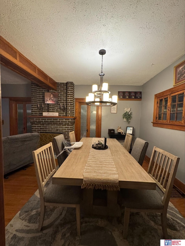 dining area featuring hardwood / wood-style flooring, a fireplace, an inviting chandelier, and a textured ceiling