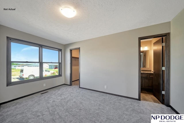 unfurnished bedroom featuring light colored carpet, ensuite bathroom, and a textured ceiling