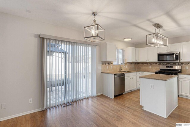 kitchen featuring white cabinetry, light wood-type flooring, a kitchen island, pendant lighting, and stainless steel appliances